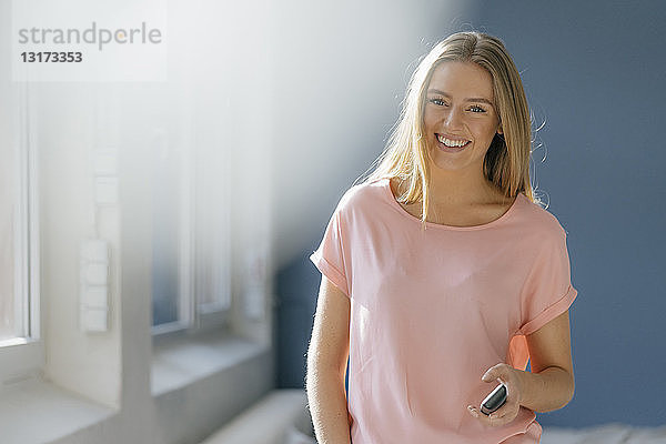 Porträt einer lächelnden jungen Frau mit Handy in der Hand