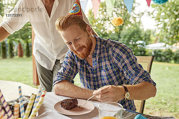 Mann isst Kuchen auf einer Geburtstagsgartenparty
