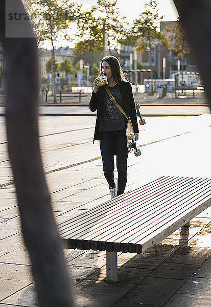 Junge Frau mit Longboard bei einem Imbiss in der Stadt