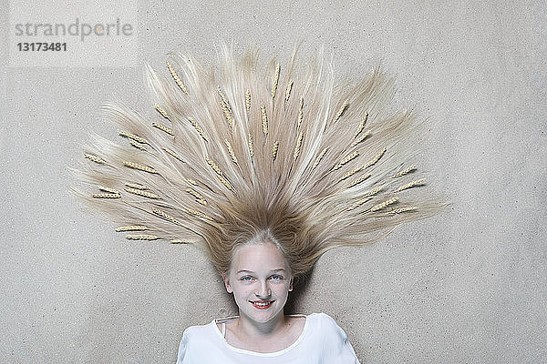 Porträt eines lächelnden Mädchens auf dem Boden liegend mit Weizenähren an den Haaren