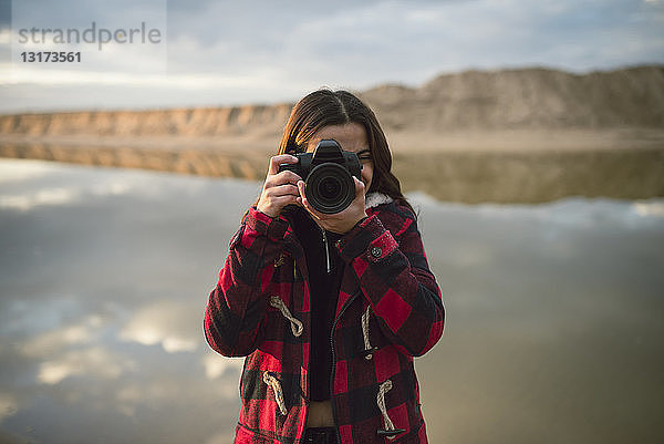 Junge Frau beim Fotografieren mit Kamera am Strand