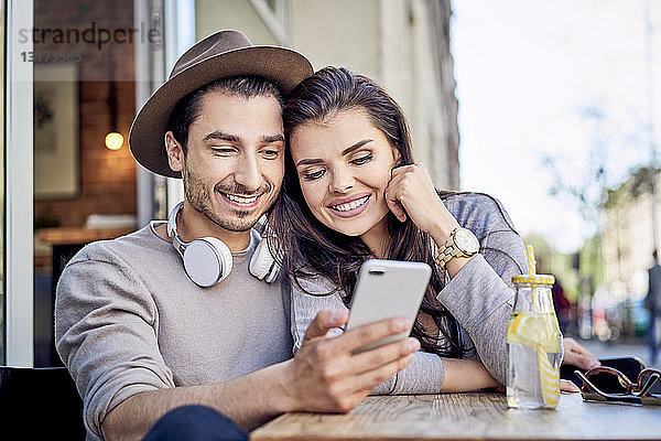 Glückliches junges Paar betrachtet Handy im Außencafé