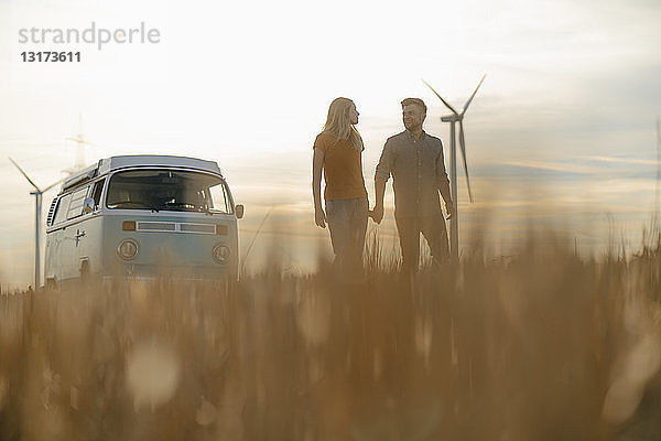 Junges Paar Hand in Hand im Wohnmobil in ländlicher Landschaft bei Sonnenuntergang