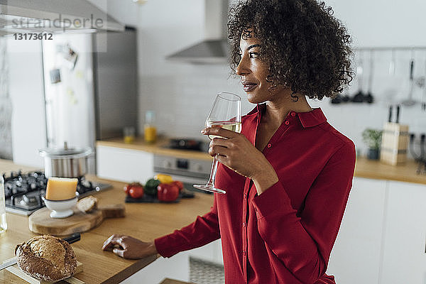 Frau steht in der Küche und trinkt ein Glas Weißwein