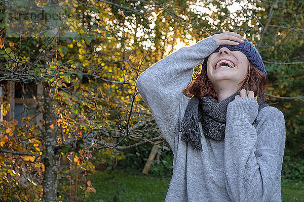 Lachendes Teenagermädchen mit Wollmütze und Schal im Herbst