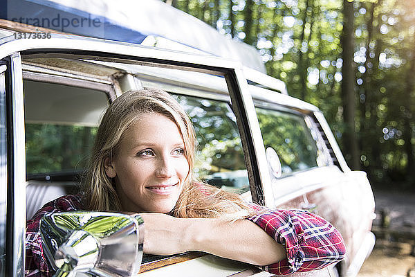 Lächelnde junge Frau im Auto im Wald
