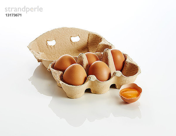 Eierschachtel mit braunen Eiern und einem geöffneten Ei auf weißem Hintergrund