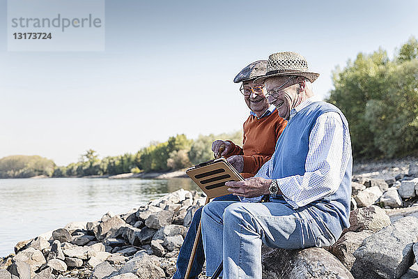 Zwei alte Freunde sitzen am Flussufer und benutzen ein digitales Tablett