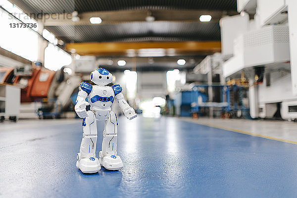 Spielzeugroboter steht auf dem Boden einer Fabrikhalle