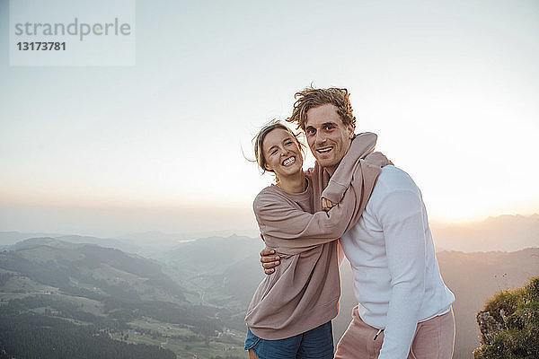 Schweiz  Grosse Mythen  Porträt eines glücklichen jungen Paares  das sich bei Sonnenaufgang in einer Berglandschaft umarmt