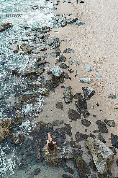 Draufsicht auf eine junge Frau  die auf einem Felsen an der Strandpromenade sitzt
