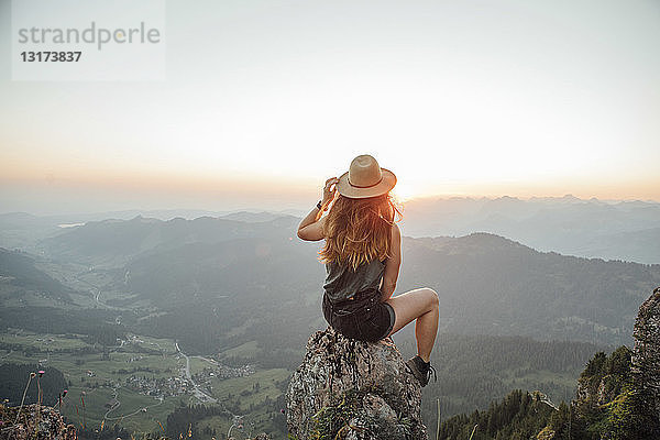 Schweiz  Grosse Mythen  junge Frau auf einer Wanderung  die bei Sonnenaufgang auf einem Felsen sitzt