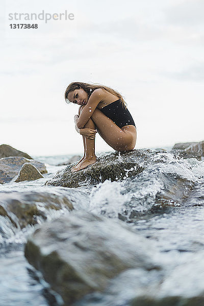 Hübsche junge Frau im Badeanzug auf einem Felsen im Meer sitzend