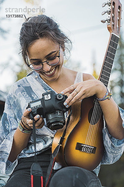 Lächelnde Frau hält Ukulele und sieht sich Bilder auf der Kamera an