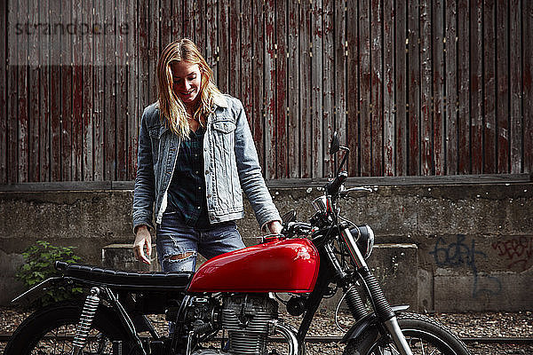 Lächelnde junge Frau steht neben dem Motorrad