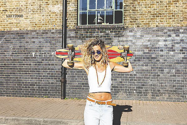 Porträt einer lächelnden jungen Frau mit Skateboard in der Stadt
