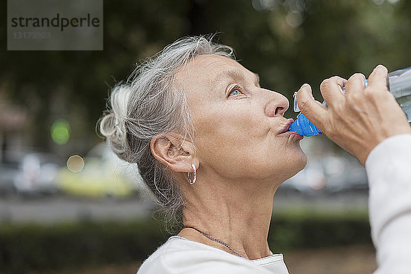 Ältere Frau im Freien trinkt Wasser aus der Flasche