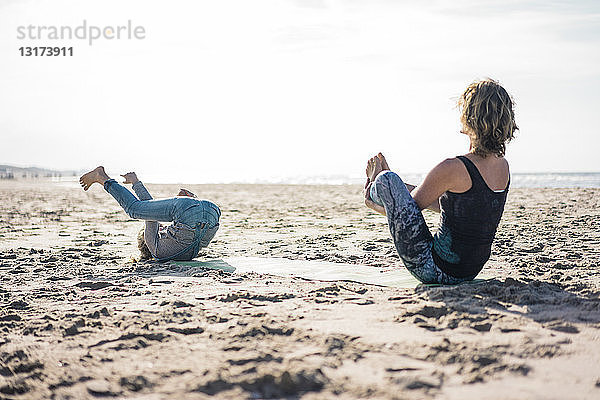 Mutter und Tochter praktizieren Yoga am Strand