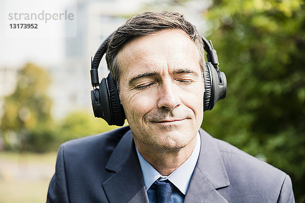 Geschäftsmann mit geschlossenen Augen  der mit Kopfhörern Musik hört