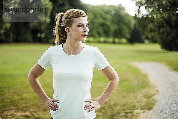 Sportliche junge Frau  die in einem Park steht und zur Seite schaut