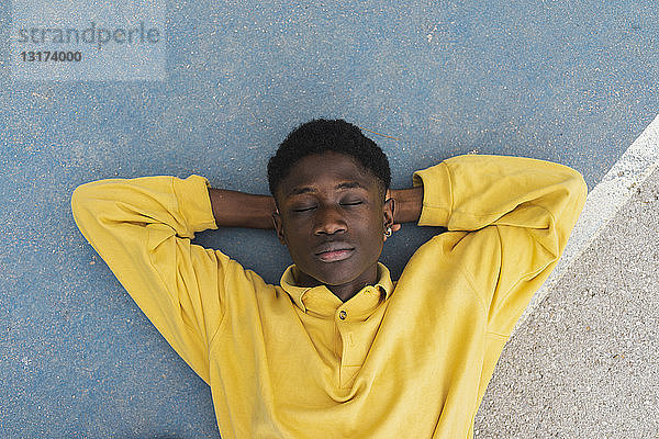Junger schwarzer Mann schläft auf dem Boden  die Hände hinter dem Kopf