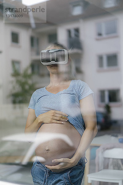 Schwangere Frau mit VR-Brille hinter der Fensterscheibe