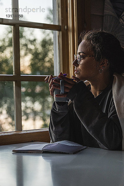 Finnland  Lappland  junge Frau sitzt am Fenster und hält einen Becher