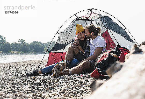 Glückliches junges Paar sitzt in einem Zelt am Flussufer