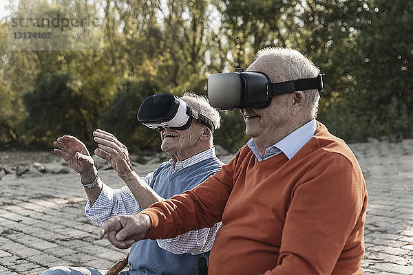 Zwei alte Freunde sitzen am Flussufer und tragen VR-Brillen