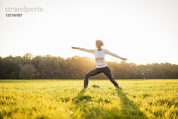 Ältere Frau macht Yoga auf einer ländlichen Wiese bei Sonnenuntergang