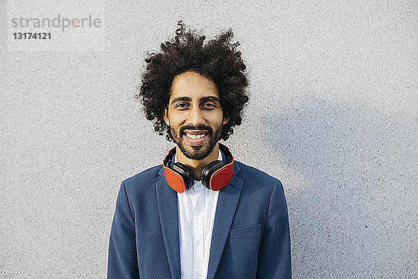Porträt eines lächelnden jungen Geschäftsmannes mit Kopfhörern an einer Wand