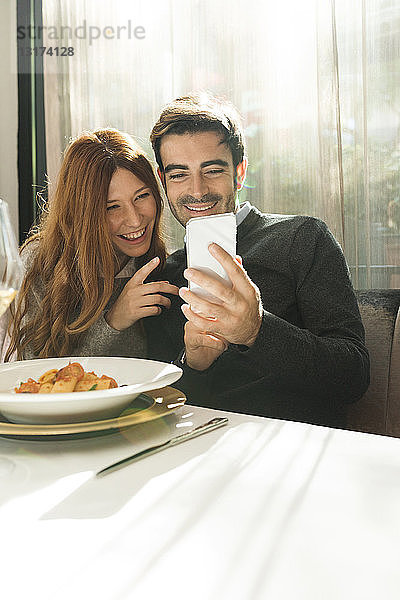 Glückliches Paar betrachtet Handy in einem Restaurant