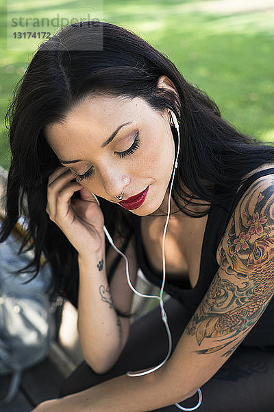Porträt einer jungen Frau mit Nasenpiercing und Tätowierungen  die mit Kopfhörern Musik hört