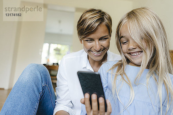 Glückliche Mutter und Tochter schauen sich gemeinsam ein Smartphone an