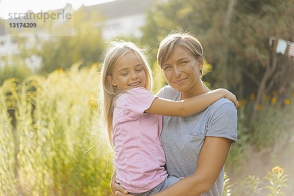 Porträt einer lächelnden Mutter  die ihre Tochter in der Natur trägt
