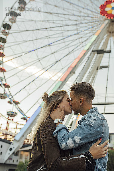 Glückliches junges Paar umarmt und küsst sich auf einer Kirmes