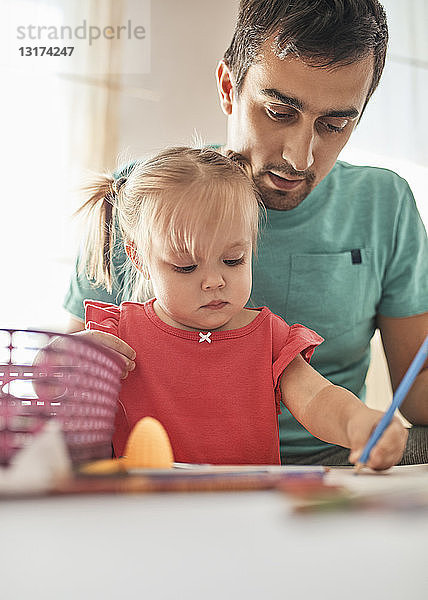 Porträt eines kleinen Mädchens  das mit Farbstift zeichnet  während ihr Vater es beobachtet
