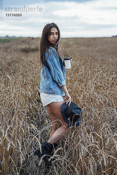 Porträt einer jungen Frau mit Getränk beim Spaziergang im Maisfeld
