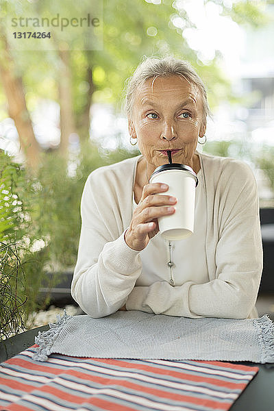 Ältere Frau mit einem Getränk in einem Außencafé