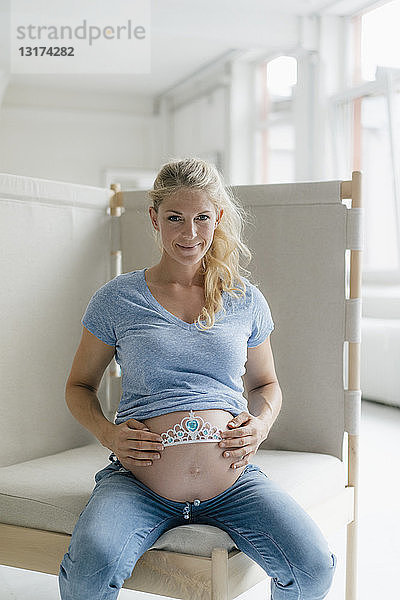 Porträt einer lächelnden schwangeren Frau  die das Diadem am Bauch hält