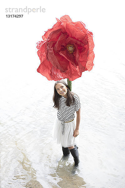 Porträt eines lächelnden Mädchens  das in einem See mit übergroßer roter Kunstblume steht