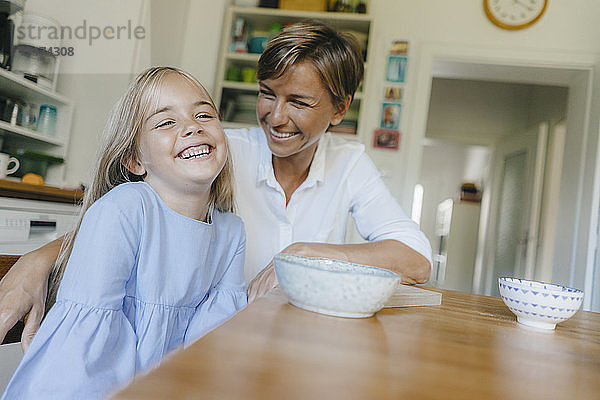 Glückliche Mutter und Tochter sitzen zu Hause am Küchentisch