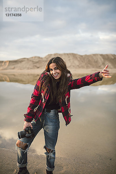 Porträt einer lachenden jungen Frau mit Kamera am Strand