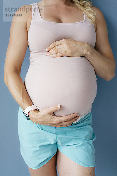 An der blauen Wand stehender Mittelteil einer schwangeren Frau