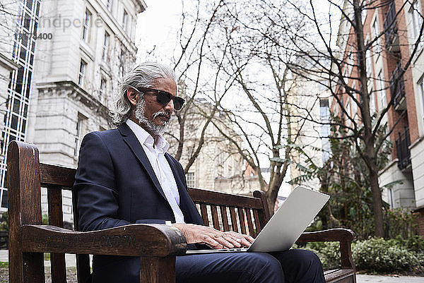 UK  London  leitender Geschäftsmann sitzt auf einer Bank im Freien und arbeitet am Laptop