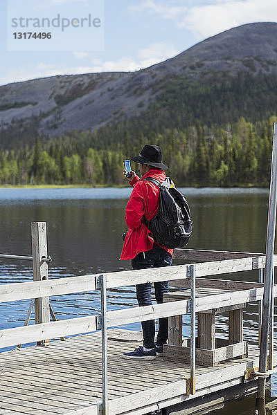 Finnland  Lappland  Mann macht Handyfoto am Seeufer
