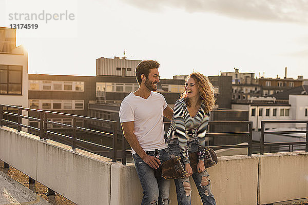 Glückliches junges Paar entspannt sich bei Sonnenuntergang auf der Dachterrasse