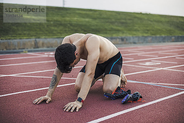 Athlet kniend auf einer Tartanbahn nach Beendigung eines Rennens