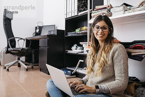 Porträt einer lächelnden jungen Frau  die zu Hause mit einem Laptop auf dem Boden sitzt