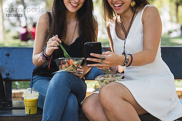 Freundinnen sitzen in einem Park und essen Salat